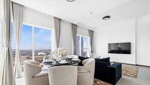 A modern living room with a city view, a round dining table, comfortable seating, and a flat-screen TV. - Luxury Suite Canal Views Infinity Pool (Dubai)