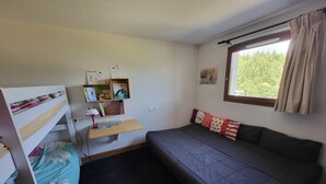 A small, cozy room with a bunk bed, a desk with a lamp, and a window with curtains. - Peaceful Mountain Apartment in Morillon (Morillon)