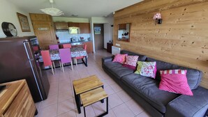 A living room with a grey sofa, wooden coffee table, and a kitchen in the background. - Peaceful Mountain Apartment in Morillon (Morillon)
