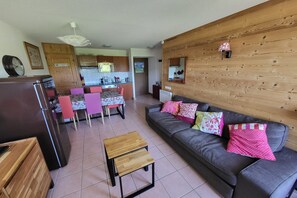 Ein Wohnzimmer mit grauem Sofa, Couchtisch aus Holz und einer Küche im Hintergrund.