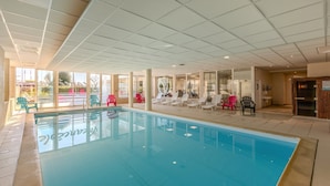 Una piscina interior con paredes de vidrio transparente, sillones de descanso y techo de azulejos.