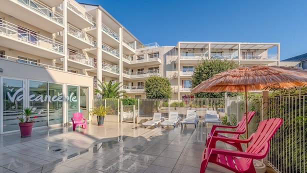 Un patio moderno de hotel con piscina, tumbonas y un restaurante llamado "Vacances".