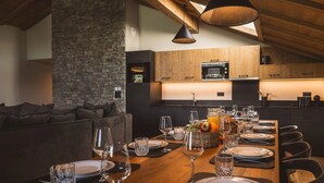 A modern kitchen with wooden cabinets, a stone accent wall, and a dining area set for six with wine glasses and plates. - Apartment in The Residence L' Éclat des  Véria (MEGEVE)