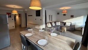 A modern living room with a wooden dining table set for four, a grey sofa, and a large window providing natural light. - Les Marmottes N°302 - 2P7 (Les Deux Alpes)
