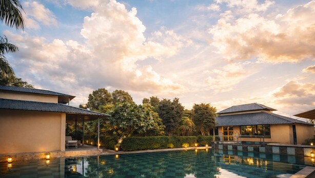 A swimming pool with a reflection of the sky and trees, surrounded by buildings with a covered patio and a view of the sky. - Rambagh Retreat-Stay with  Swimming Pool (Udaipur)