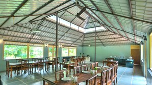 A spacious dining hall with high ceilings and large windows, featuring wooden tables and chairs, and a central counter area. - Rambagh Retreat-Stay with  Swimming Pool (Udaipur)