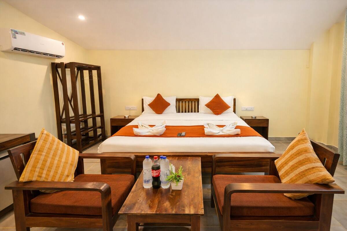 A hotel room with a bed, two wooden chairs, a small table with bottles and a plant, and a wardrobe.