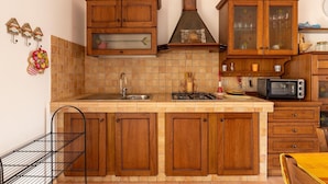 A kitchen with wooden cabinets, a gas stove, a sink, and a microwave. - With air conditioning and private terrace (Castelsardo)