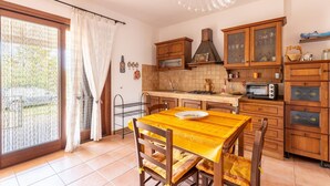 A kitchen with wooden cabinets, a dining table with yellow tablecloth, and a view through a sliding glass door. - With air conditioning and private terrace (Castelsardo)
