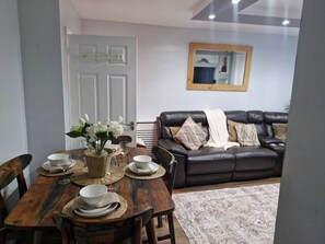 A dining area with a wooden table set for four, surrounded by chairs. A white door with a handle is visible in the background.