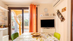 A dining area with a table set for two, a television, and a wine rack. - Aria condizionata e ampio spazio esterno (Castelsardo)