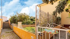 A gated entrance with a sign reading "Welcome to Paradise," a cobblestone path, and a staircase leading to a building. - Aria condizionata e ampio spazio esterno (Castelsardo)