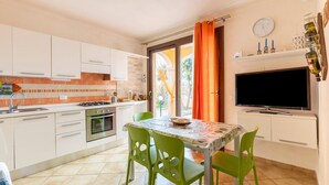A compact kitchen with white cabinets, a gas stove, and a dining area with a table and chairs. - Aria condizionata e ampio spazio esterno (Castelsardo)
