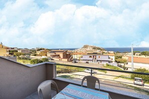 En balkon med et bord og stole, med udsigt over et boligområde med huse og en bakke i det fjerne.