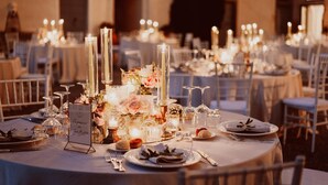 En festlokal med runda bord uppdukat för ett formellt evenemang, med vackra glas, ljus och blomsterarrangemang som dekoration.