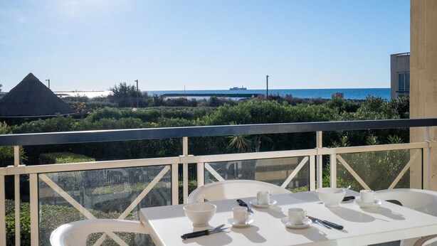 Un balcón con una mesa dispuesta para dos personas, con vista a una zona costera con vegetación y una vista despejada del mar.