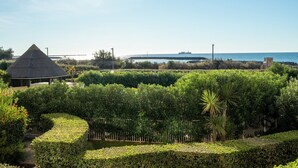 Un jardín ajardinado con una estructura de techo de paja, setos perfectamente cuidados y vistas al mar y un puente distante.