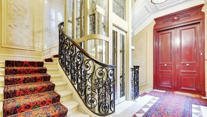 A grand staircase with ornate black railings, a red door, and patterned carpet.