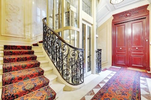 A grand staircase with ornate black railings, a red door, and patterned carpet.