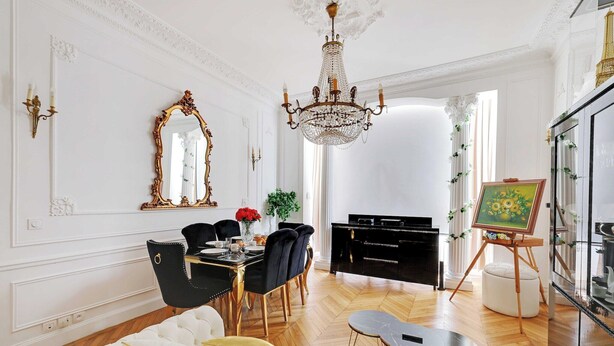 A dining area with a chandelier, a piano, and a painting on easels.