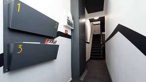 Un pasillo con tres taquillas numeradas, un detector de incendios y una escalera que sube a otro piso.