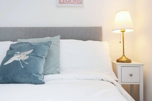 A neatly made bed with white and teal pillows, a gold lamp on a bedside table, and a framed sign on the wall. - Luxury Living, Central Spot (Cardiff)