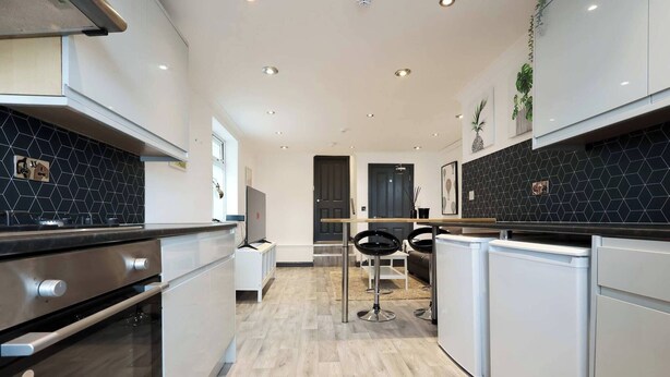 Una cocina moderna con salpicadero de azulejos negros, electrodomésticos de acero inoxidable y piso de madera clara.