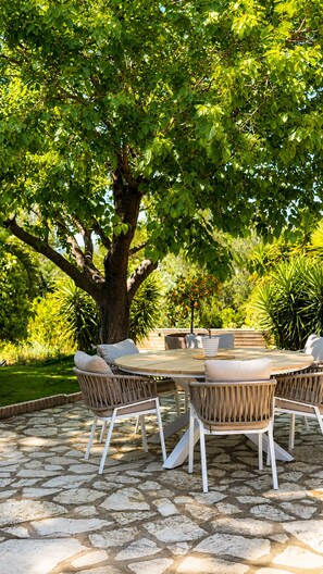 Un espace extérieur aménagé pour les repas, avec une table ronde et des chaises en osier, entouré d’une terrasse en pierre.