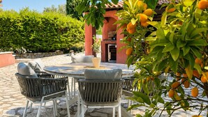 Eine Terrasse im Freien mit Steinboden, einem runden Tisch mit Stühlen und einem Topf mit gelb fruchttragenden Pflanzen.