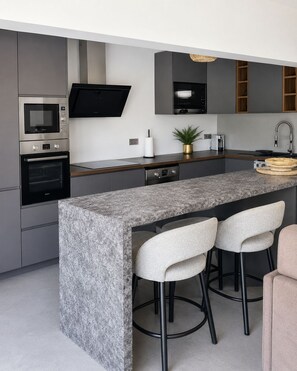 Une cuisine moderne dotée d’un comptoir en granit, d’appareils électroménagers en acier inoxydable et de tabourets de bar.