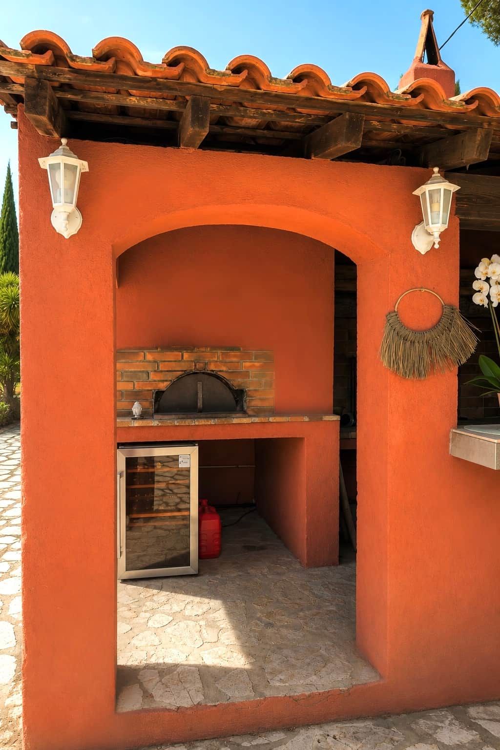 An outdoor brick oven with a stone floor, surrounded by a wall painted in a warm color.