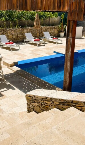 A pool area with lounge chairs and a stone wall.