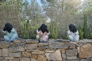 Drei Statuen von Kindern sitzen auf einer Steinmauer, im Hintergrund ist ein Bambuszaun zu sehen.