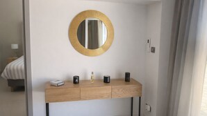 Ein modernes Badezimmer mit einem hölzernen Waschtisch, einem runden Spiegel mit goldener Rahmung und einem kleinen Nachttisch mit Lampe.