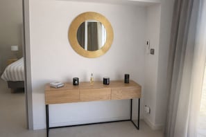 Een moderne badkamer met een houten wastafelmeubel, een ronde spiegel met gouden lijst en een klein nachtkastje met lamp.
