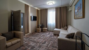 A hotel room with a sofa, a chair, a small table, a TV, and a painting on the wall. - Sapar Deluxe Plaza (Almaty)
