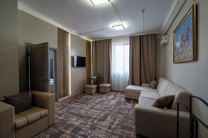Ein Hotelzimmer mit einer Couch, einem Sessel, einem kleinen Tisch, einem Fernseher und einem Bild an der Wand.