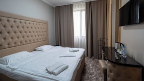 A hotel room with a large bed, a flat-screen TV, a desk with a chair, and a window with curtains. - Sapar Deluxe Plaza (Almaty)