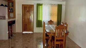 Zona de menjador amb taula i cadires de fusta, espai cuina amb barra i armaris, i una porta de fusta.