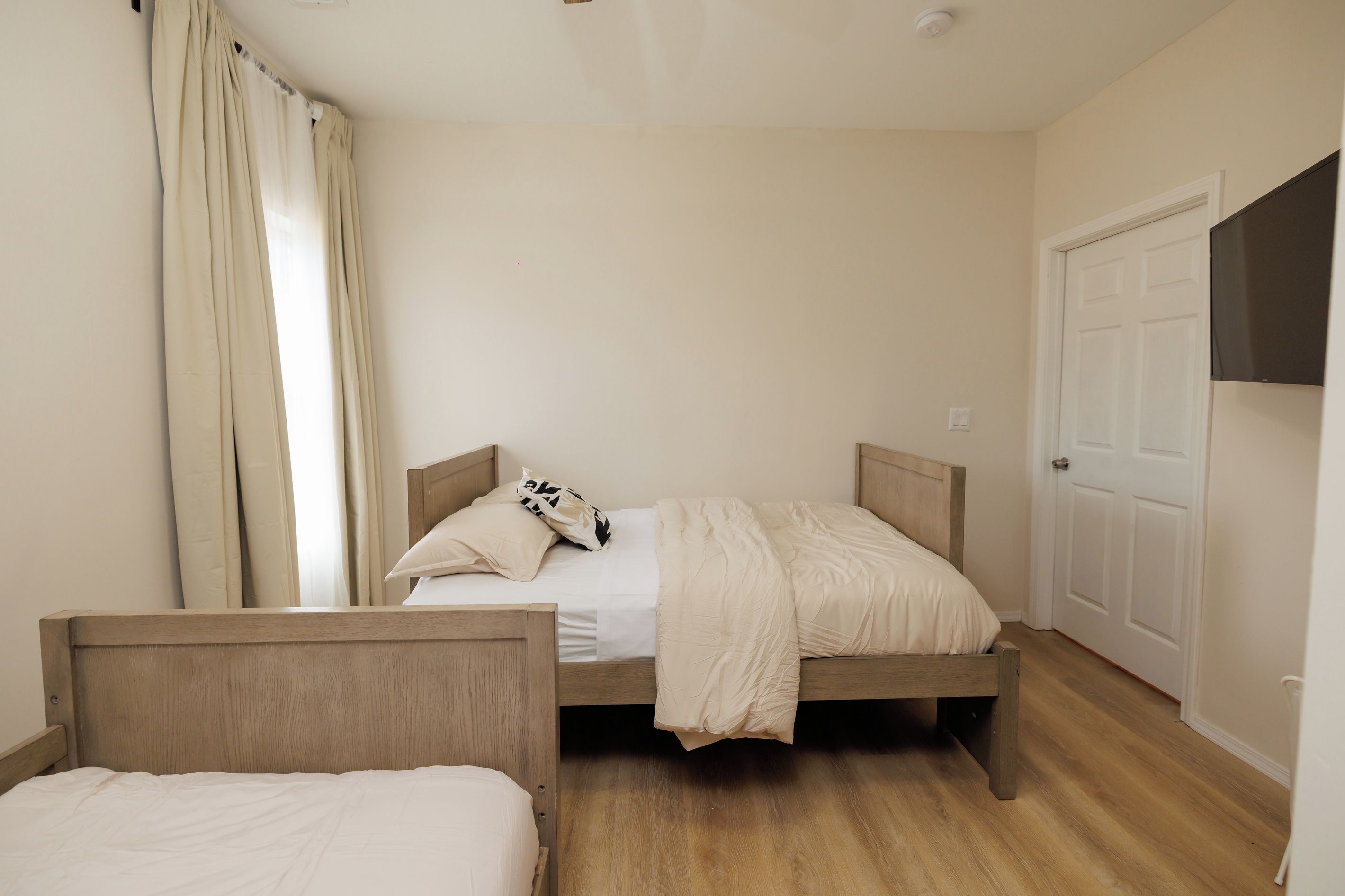 Un dormitorio con dos camas de madera, una puerta blanca y una ventana con cortinas.