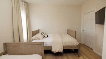 Un dormitorio con dos camas de madera, una puerta blanca y una ventana con cortinas.