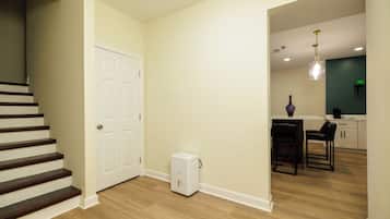 Una escalera que lleva a una puerta, un electrodoméstico pequeño y blanco, y una zona de cocina con una mesa y sillas.