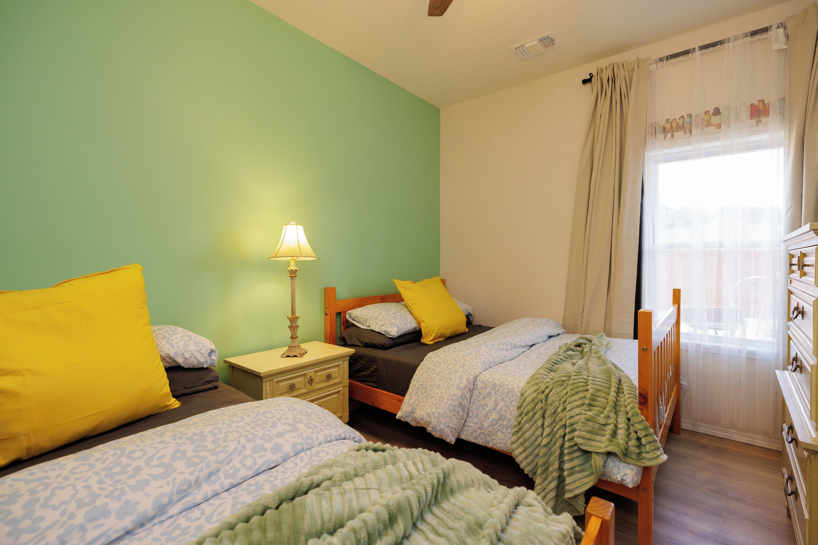 A room with two beds, a nightstand, a lamp, and a window with curtains.