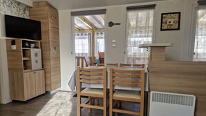 Un salon comprenant une table à manger en bois, des chaises, un téléviseur et un coin cuisine.