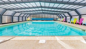 Une piscine dotée d’un toit en verre, entourée de chaises aux couleurs vives.