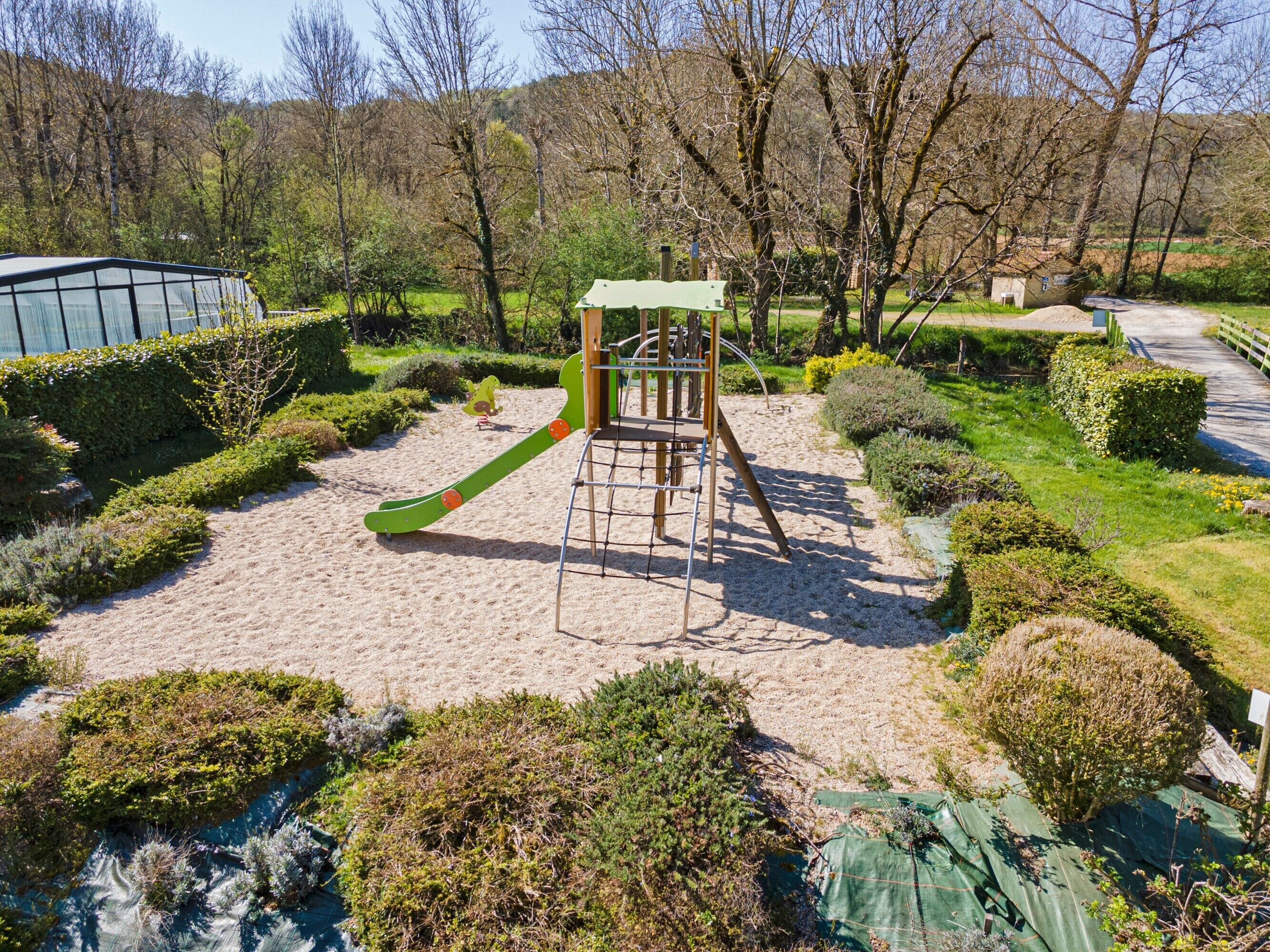 Un terrain de jeux équipé d’un toboggan et de structures d’escalade, entouré d’arbustes bien entretenus et bordé d’un chemin dégagé.
