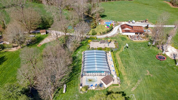 Vue aérienne d’une propriété comprenant une grande serre, une piscine et une pelouse bien entretenue.