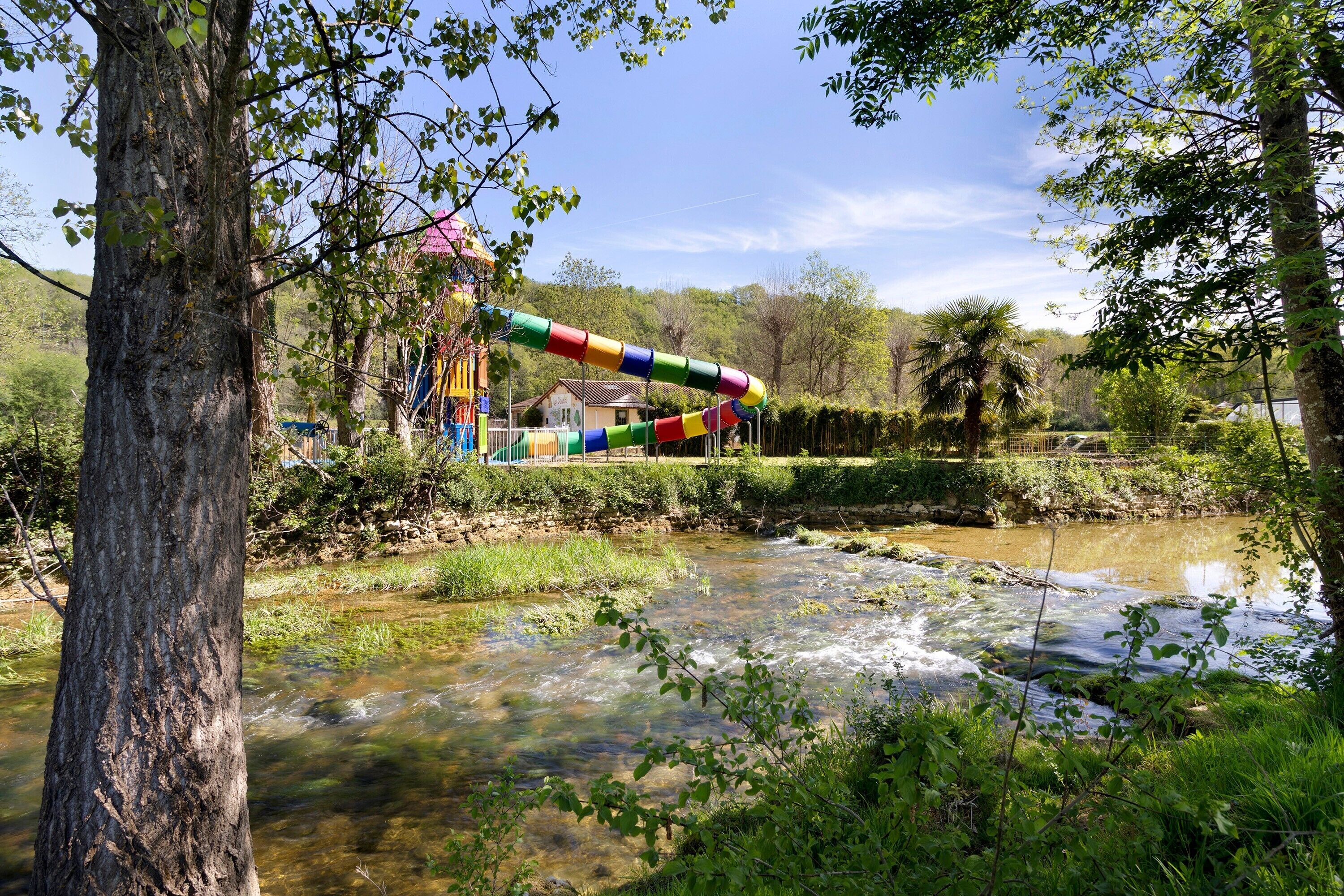 A river with a colorful slide structure, surrounded by trees and greenery.