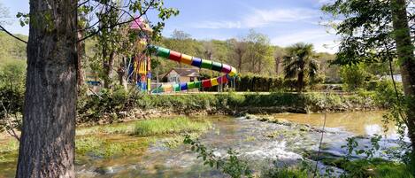 A river with a colorful slide structure, surrounded by trees and greenery.