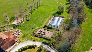 Vista aérea de una propiedad con un gran campo verde, un edificio de techo curvo y un pequeño estanque.